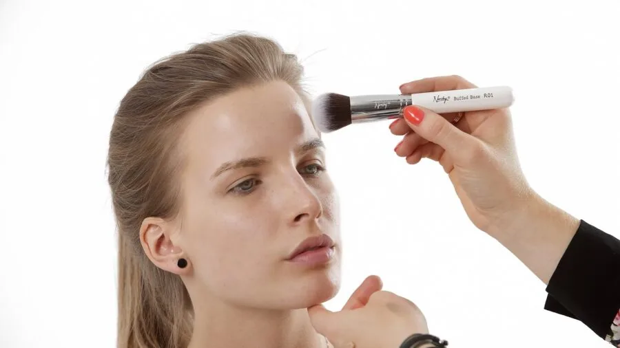 Woman applying concealer makeup in natural daylight, focusing on skin texture and finish