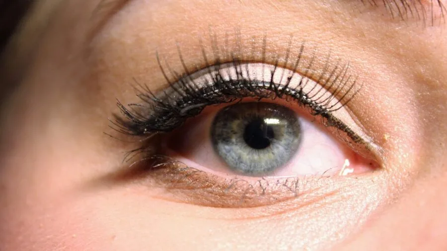 Woman applying false eyelashes in front of a mirror during makeup routine