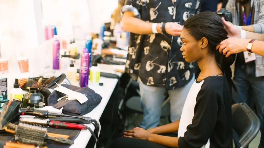 Woman applying makeup in natural light, examining finish and wearability in mirror
