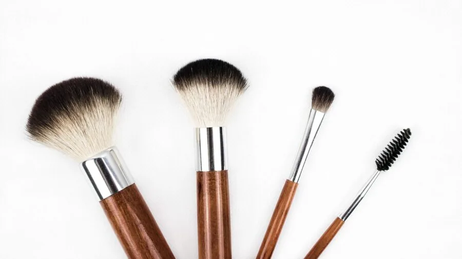 Woman applying makeup with flat brush to cheeks, demonstrating makeup application technique