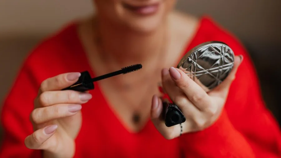 Woman applying mascara while looking in mirror during her daily beauty routine