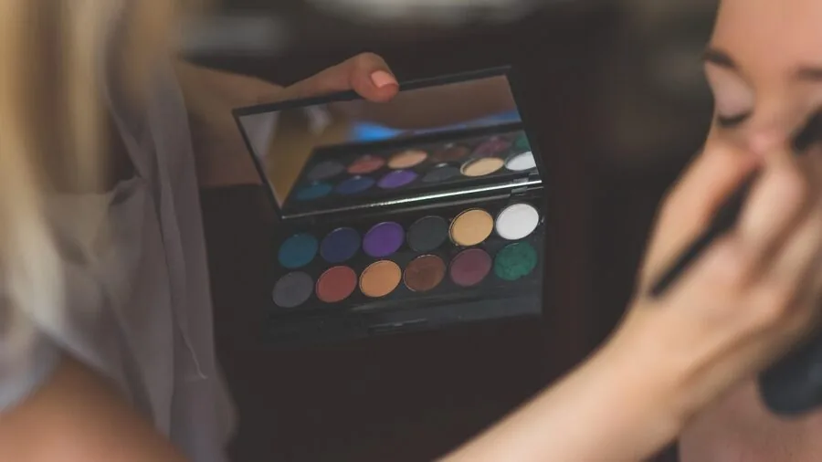 Woman applying matte eyeshadow to eyelid while looking in mirror during makeup routine