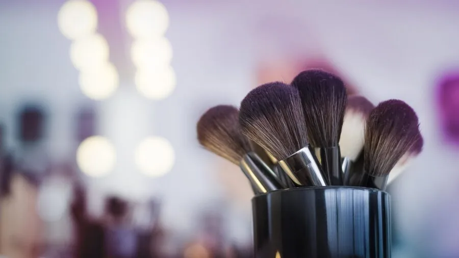Woman applying powder blush to cheeks during makeup routine with natural lighting