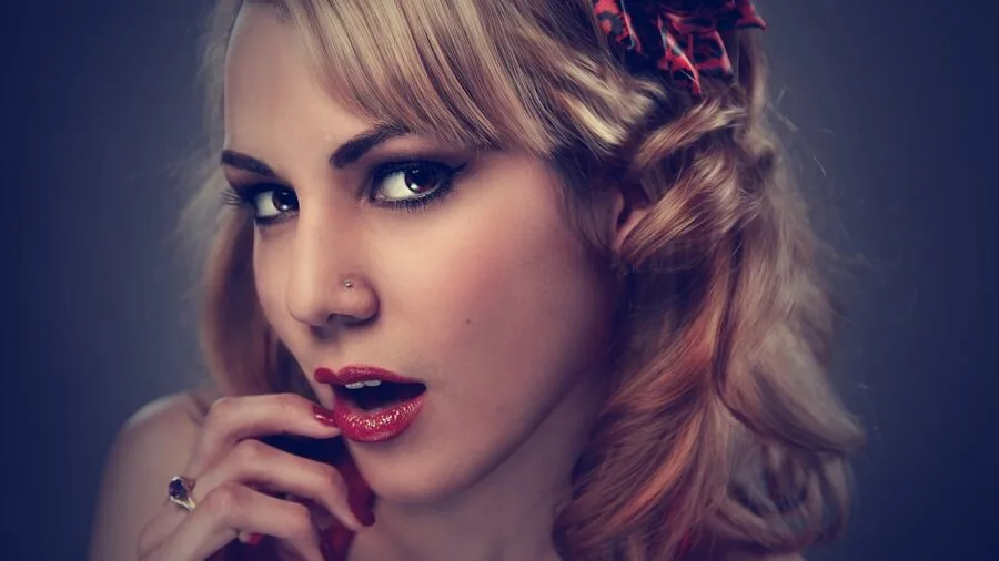 Woman applying vibrant lipstick while looking in mirror, showcasing rich color payoff and pigmentation