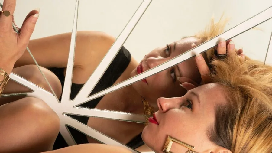 Woman carefully applying strip lashes with adhesive glue while looking in mirror during beauty routine
