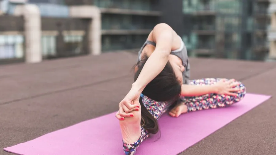 Woman carrying rolled yoga mat while walking to fitness class outdoors