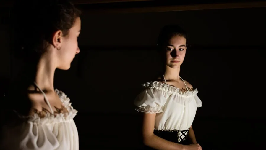 Woman checking fit of clothing in mirror, examining how garment fits her body in fitting room