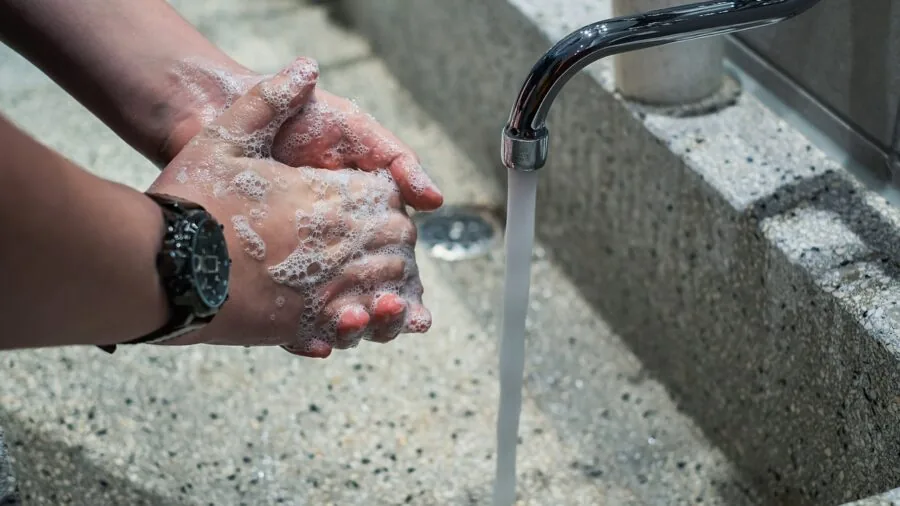 Woman cleaning dishes in a bright kitchen sink with warm water and soap