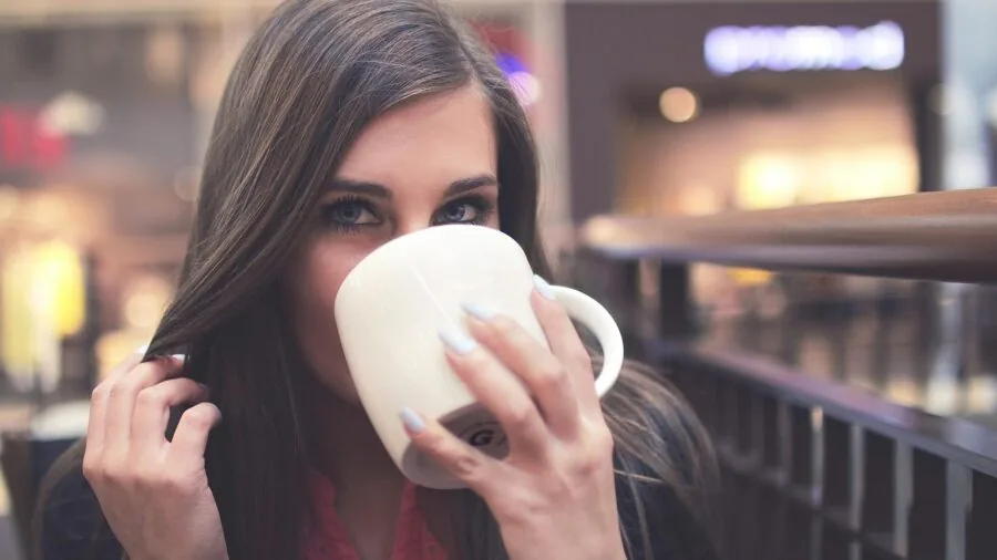 Woman enjoying beverage from travel mug while on outdoor adventure, demonstrating leak-resistant lid functionality