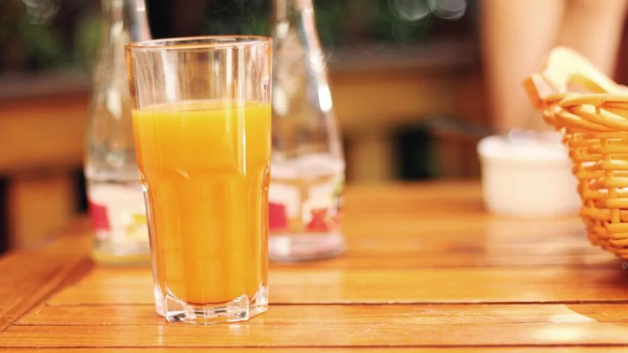 Woman enjoying fresh orange juice at breakfast table in natural sunlight