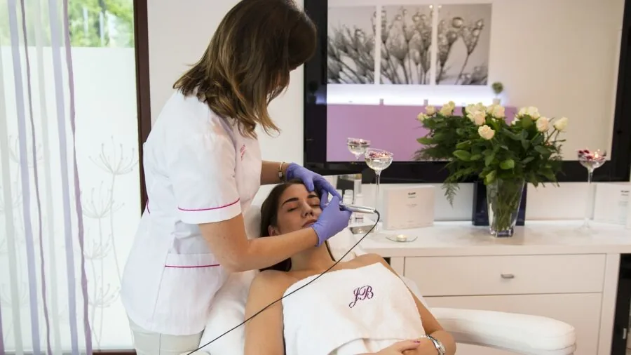 Woman in bathroom applying facial treatment to skin, demonstrating at-home beauty device usage
