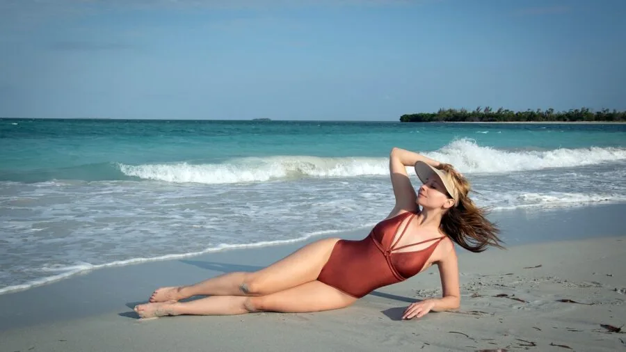 Woman in one-piece swimsuit enjoying beach day with ocean and sand in background