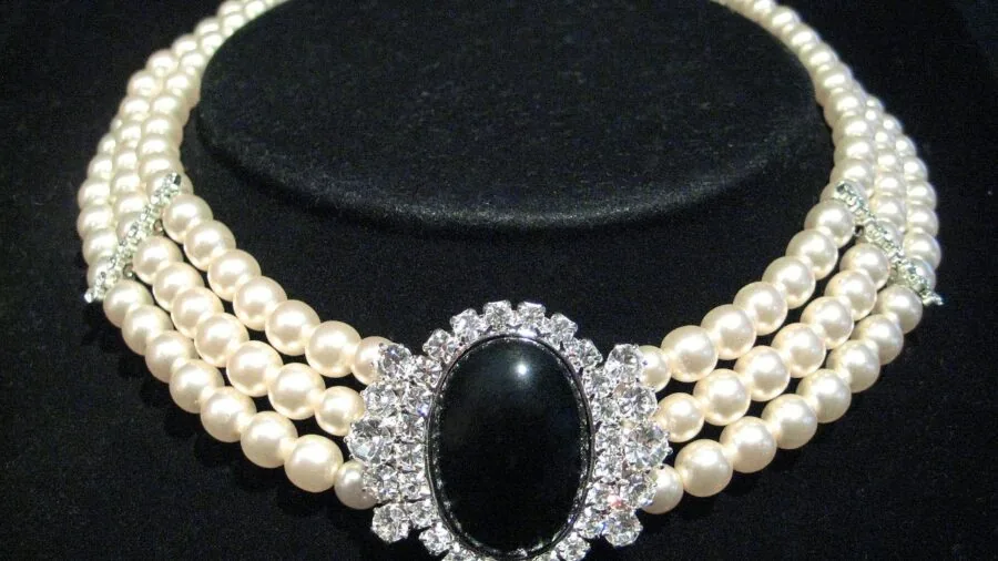 Woman inspecting pearl necklace details, evaluating quality and authenticity in natural lighting
