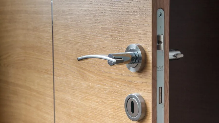 Woman opening wooden wardrobe doors in bedroom, examining clothing inside modern bedroom space
