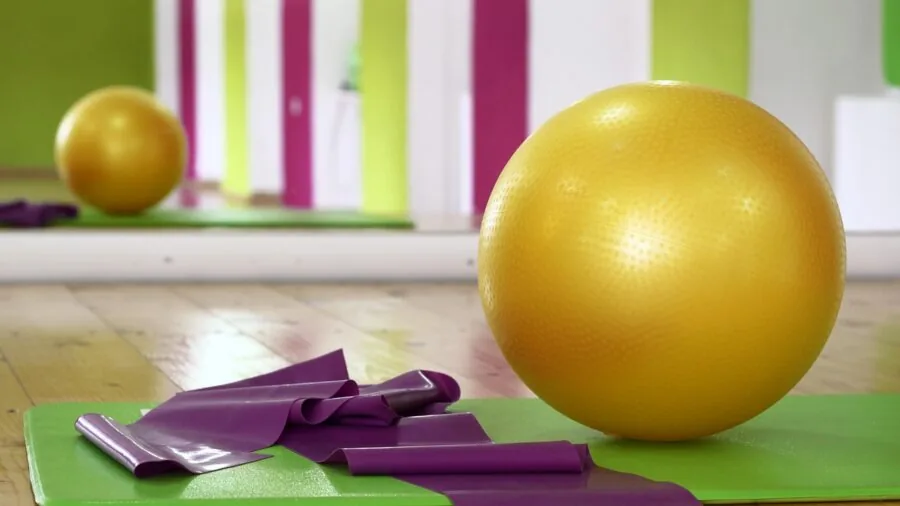 Woman performing pilates exercises with multiple fitness tools on yoga mat in bright studio space