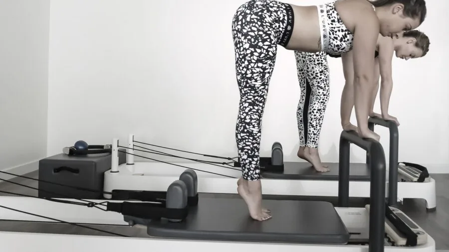 Woman performing pilates reformer exercise using footbar during indoor workout session