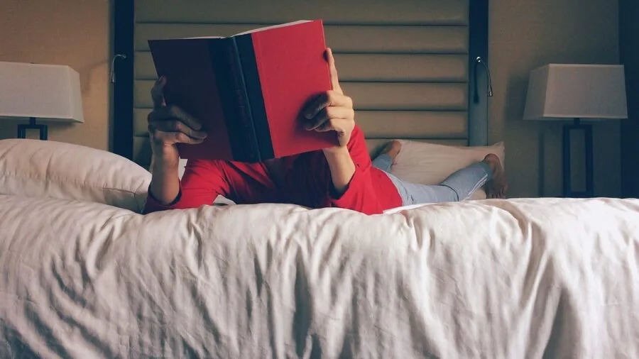 Woman reading a book in bed with comfortable padded headboard and cushions for back support