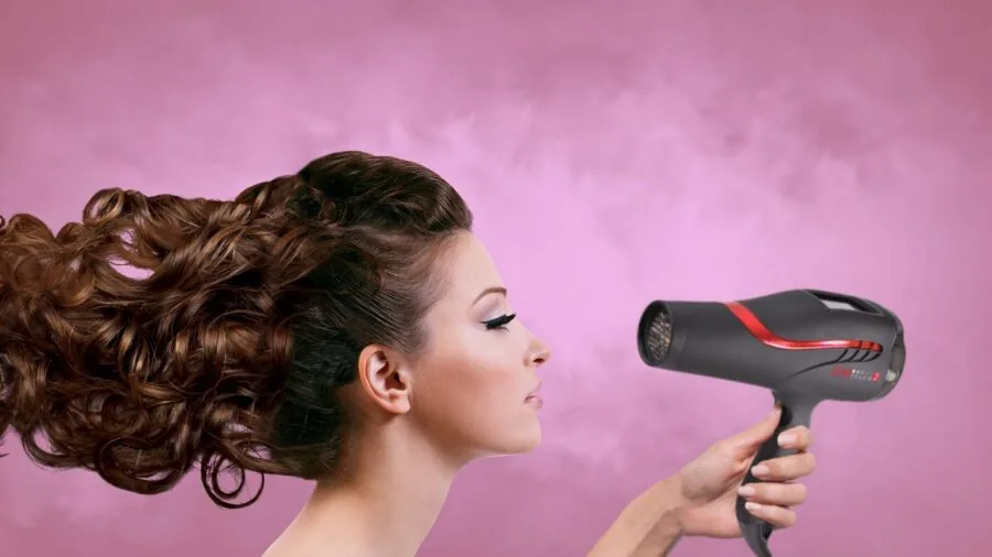 Woman using a blow dryer to style her hair with focus on heat and control settings during morning routine