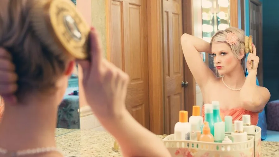 Woman using hair dryer at bathroom mirror, focusing on hair care routine and styling technique