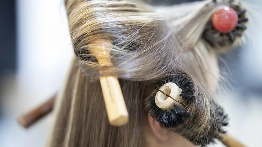 Woman using hot air brush to style long hair at home, focused on hair care routine