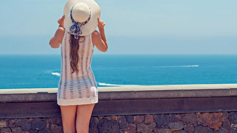 Woman wearing oversized sunglasses enjoying sunny beach day with ocean backdrop