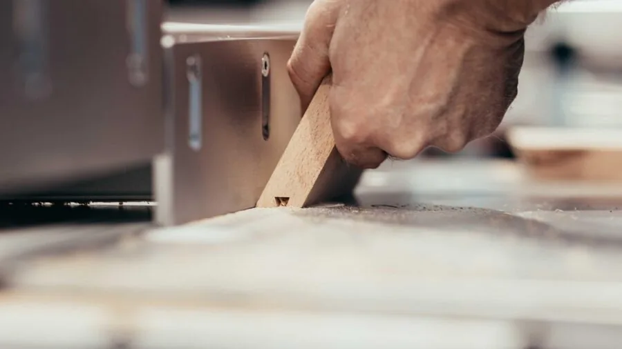 Woodworker making precise angled cuts on wood with professional tools in a workshop setting