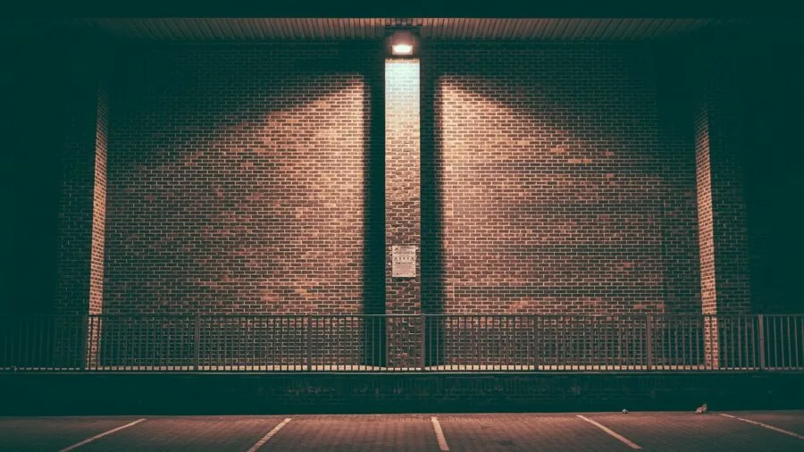 Worker in high-visibility gear walking through indoor warehouse or parking area in daytime