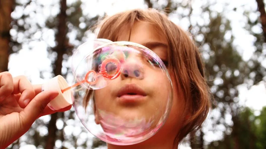 Young child blowing bubbles outside on a sunny day with natural lighting and outdoor setting