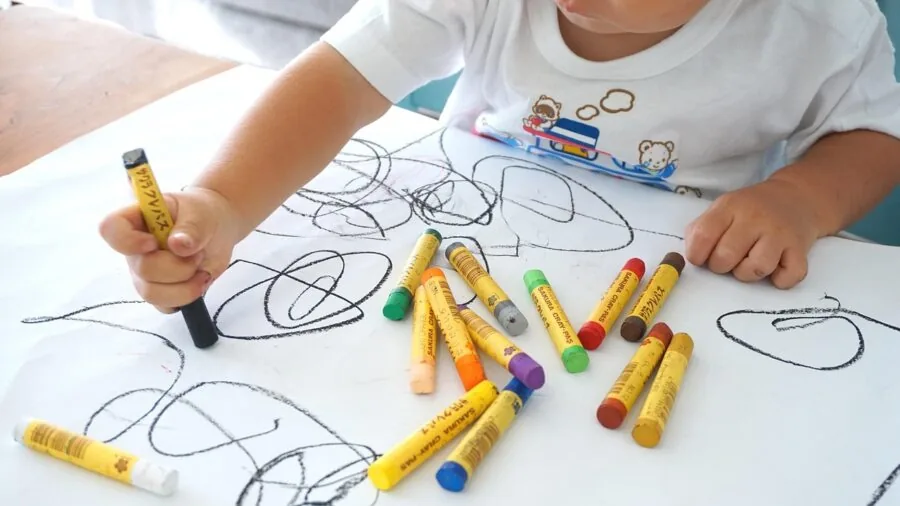 Young child coloring with a broken crayon on paper, showing typical wear from enthusiastic artistic play