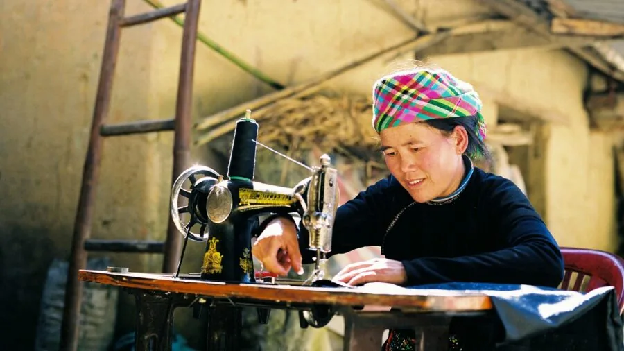 Young child concentrating while hand-sewing fabric at a wooden table with natural lighting
