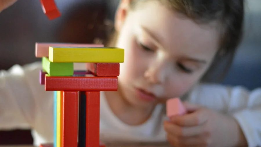 Young child concentrating while stacking colorful magnetic building blocks into a tall structure