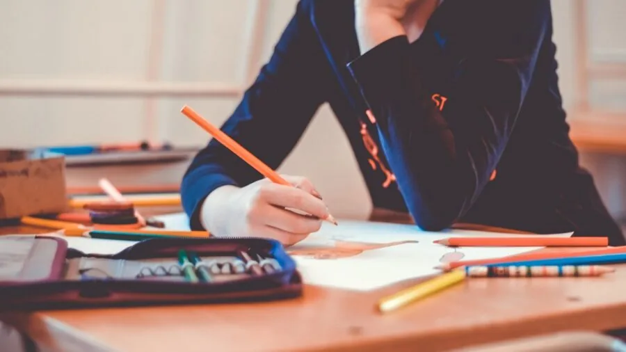 Young child drawing and sketching with colored pencils on paper at a table