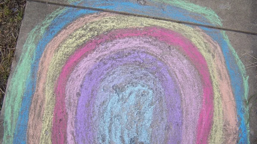 Young child drawing colorful art on sidewalk with large chalk pieces