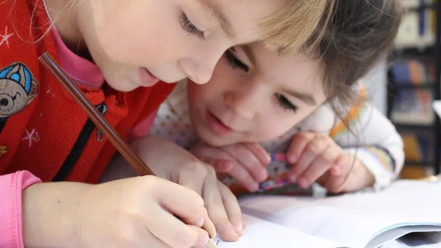 Young child drawing in a sketchbook while sitting outdoors on grass