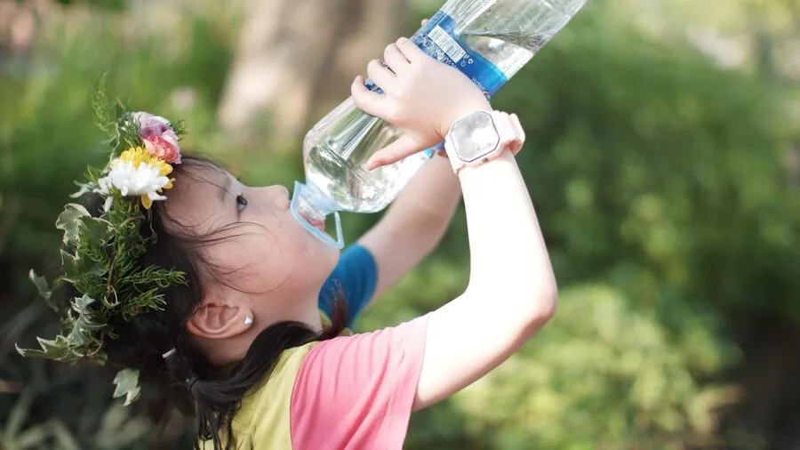 Young child drinking from a water bottle during outdoor activity, focused on hydration and daily use