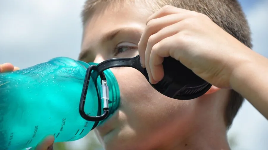 Young child enjoying a cold drink during outdoor summer activity on a sunny day