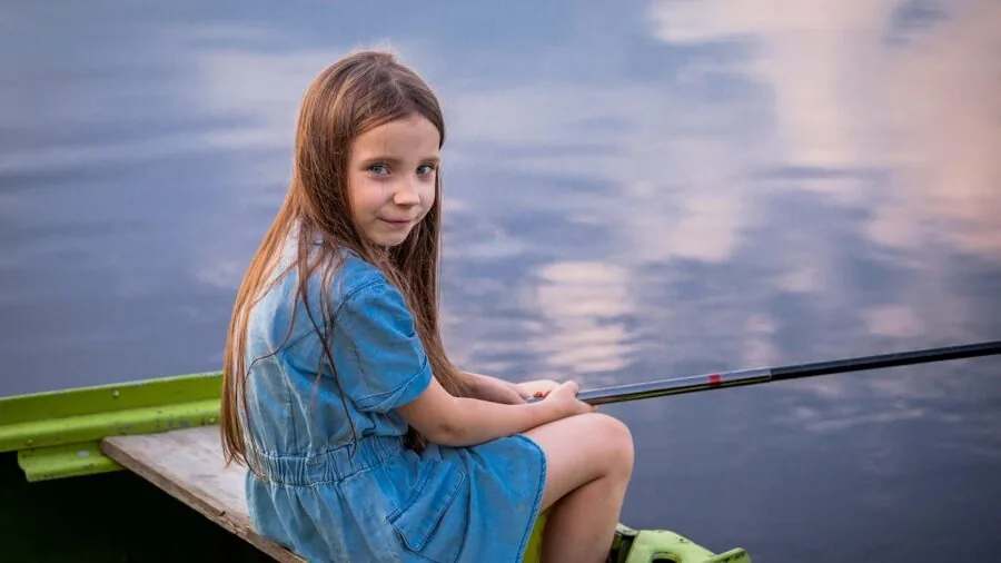 Young child enjoying fishing by the water on a sunny day, engaged in outdoor activity