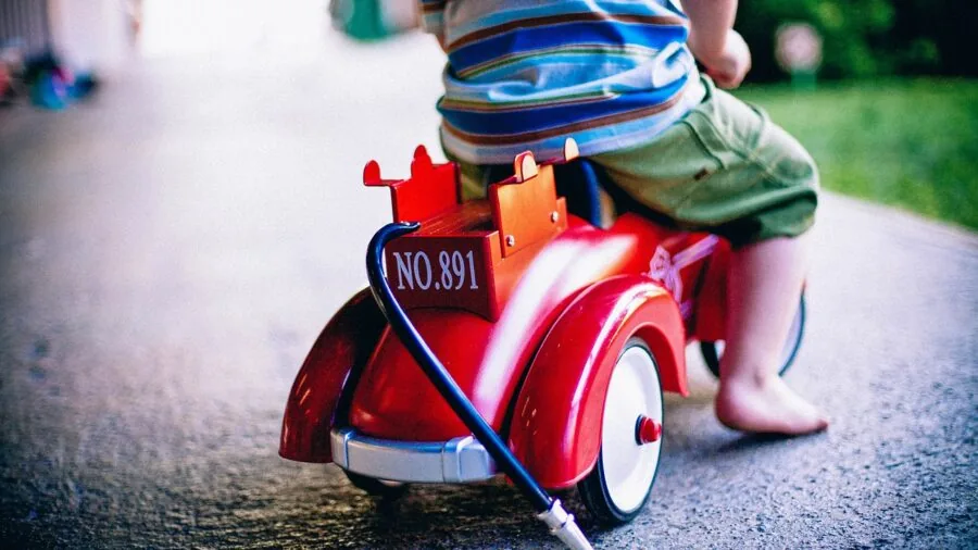 Young child enjoying playtime with a ride-on toy car in a sunny backyard setting