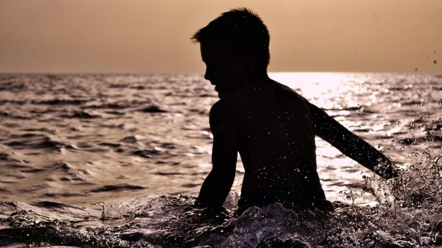 Young child enjoying water play outdoors on a sunny day, wearing colorful swimwear