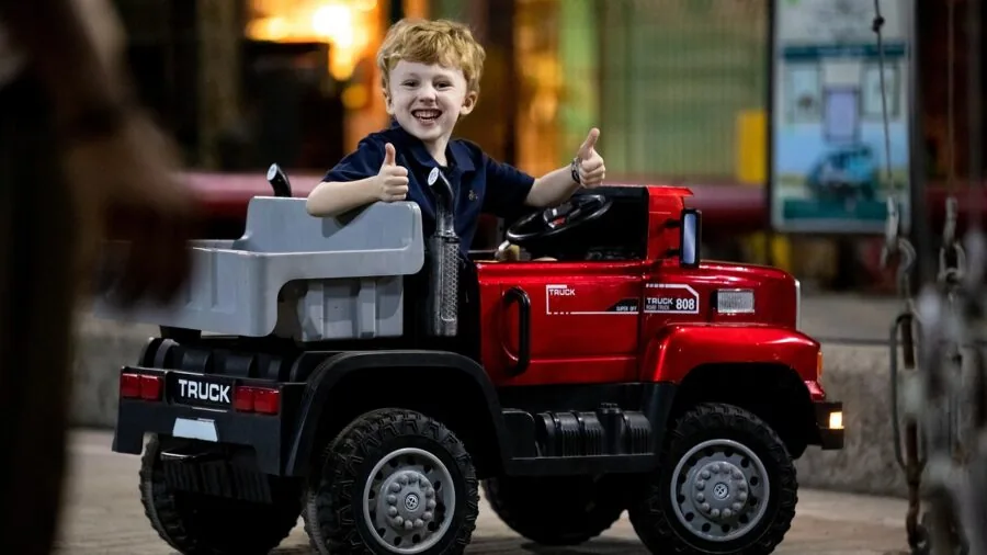 Young child enthusiastically playing with toy truck outdoors on dirt ground, demonstrating rugged play