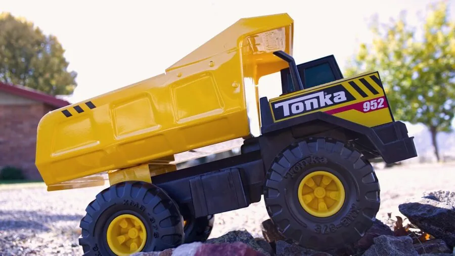 Young child examining and playing with a sturdy toy truck on wooden floor, demonstrating material durability and quality