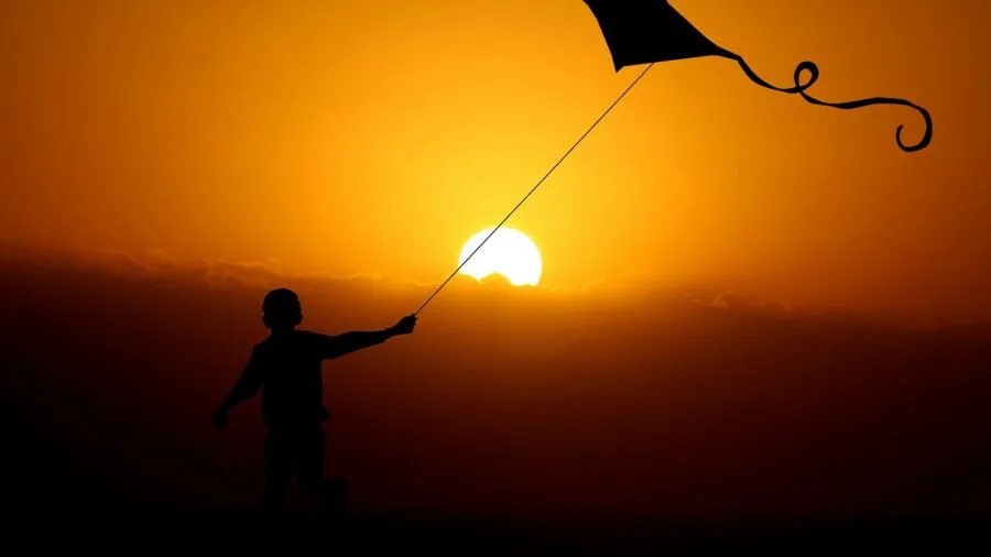Young child flying kite in open field on sunny day, beginner kite flying outdoors