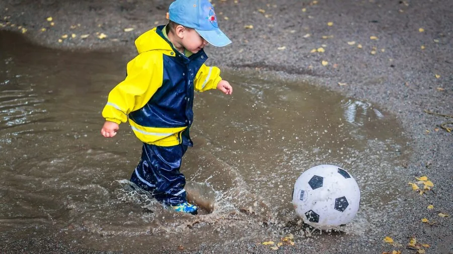 Young child in rain boots jumping in puddles outdoors on wet ground