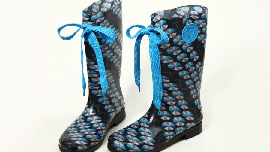 Young child independently pulling on colorful rain boots with handles, learning to dress themselves outdoors