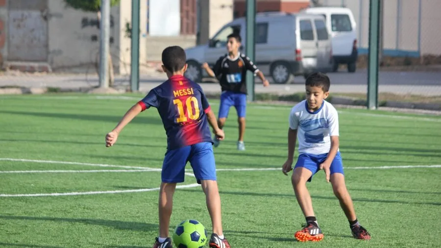 Young child kicking soccer ball toward goal in outdoor field during daytime