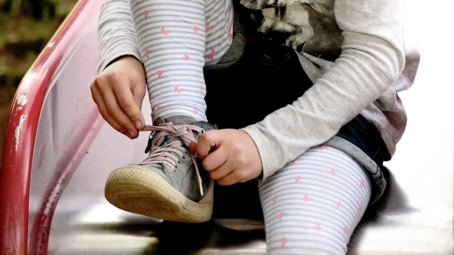 Young child learning to tie shoelaces and fasten sneakers independently while getting dressed
