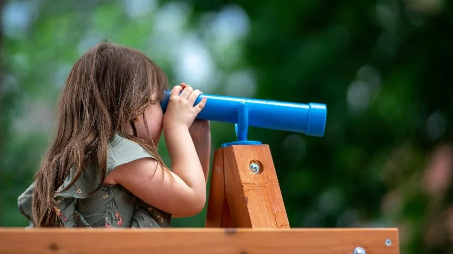 Young child looking through telescope at starry night sky outdoors