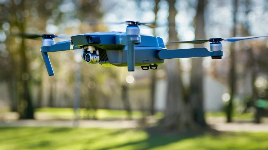 Young child operating a remote control drone in an open park during daytime with clear sky