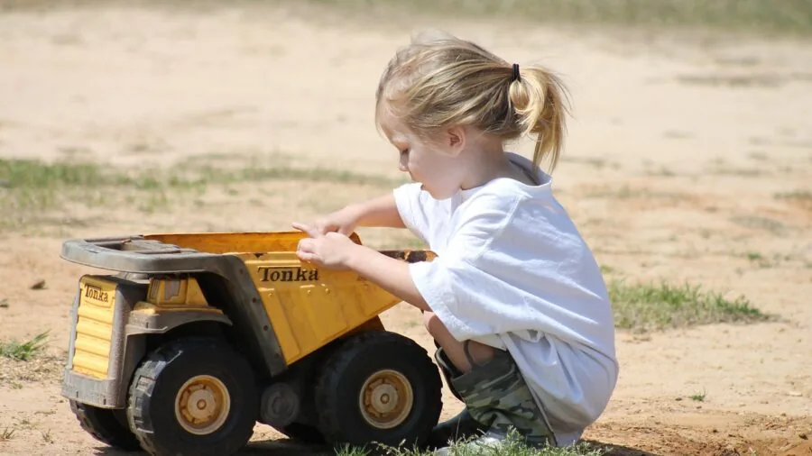 Young child operating a small RC truck in a backyard setting on grass