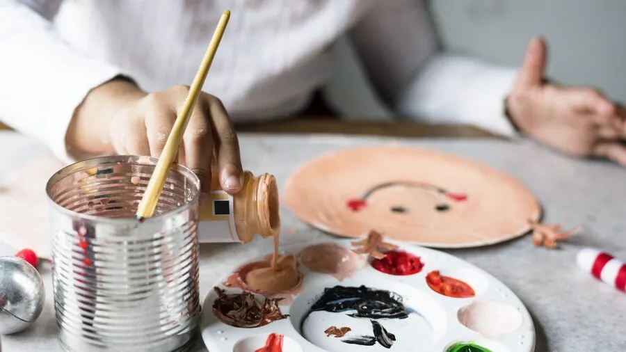 Young child painting with colorful acrylic paints at a wooden table during a creative art activity